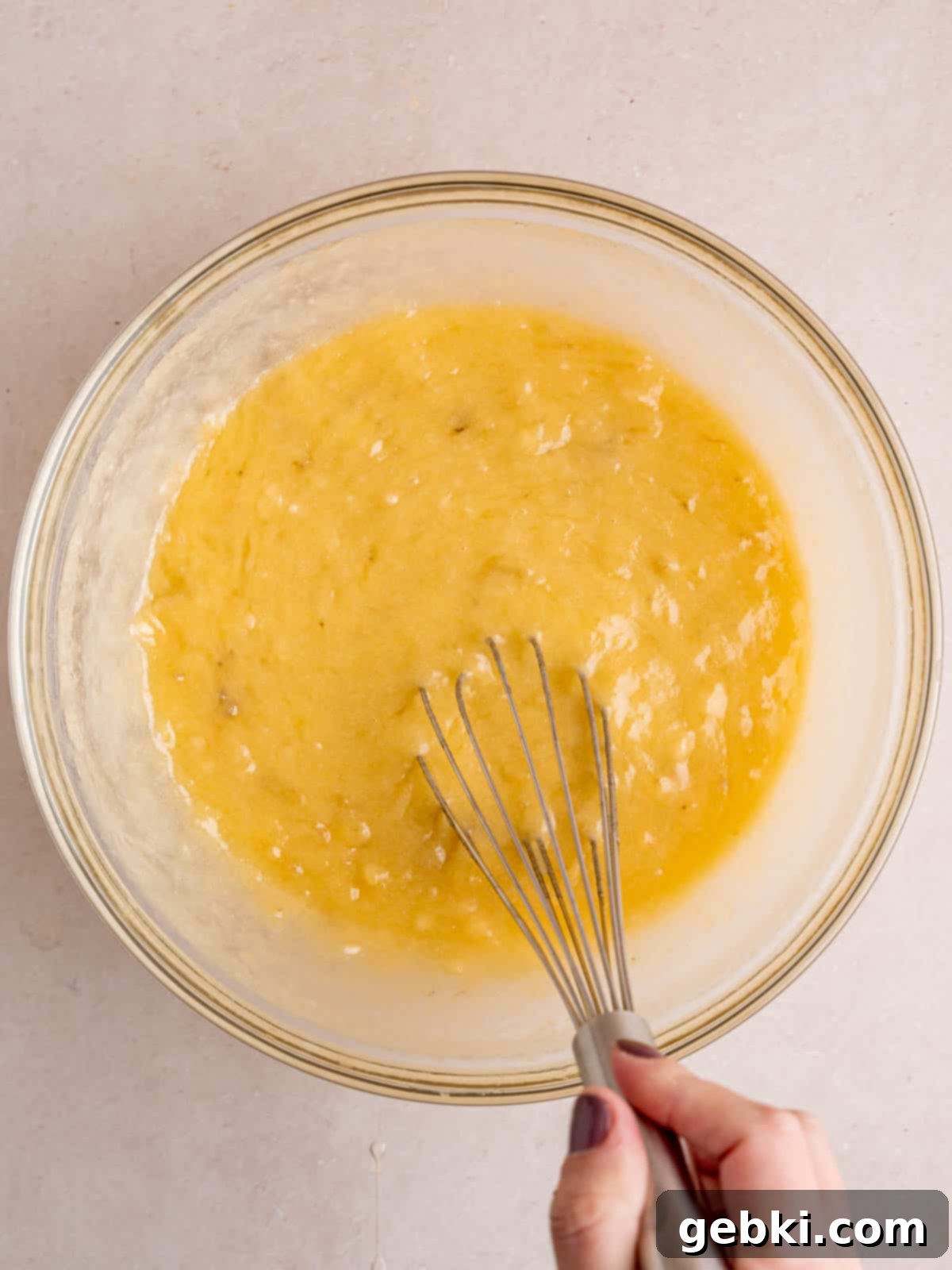 Effortless One-Bowl Banana Bread 5 Mixing mashed bananas, melted butter, sugar, and eggs in a bowl with a whisk.