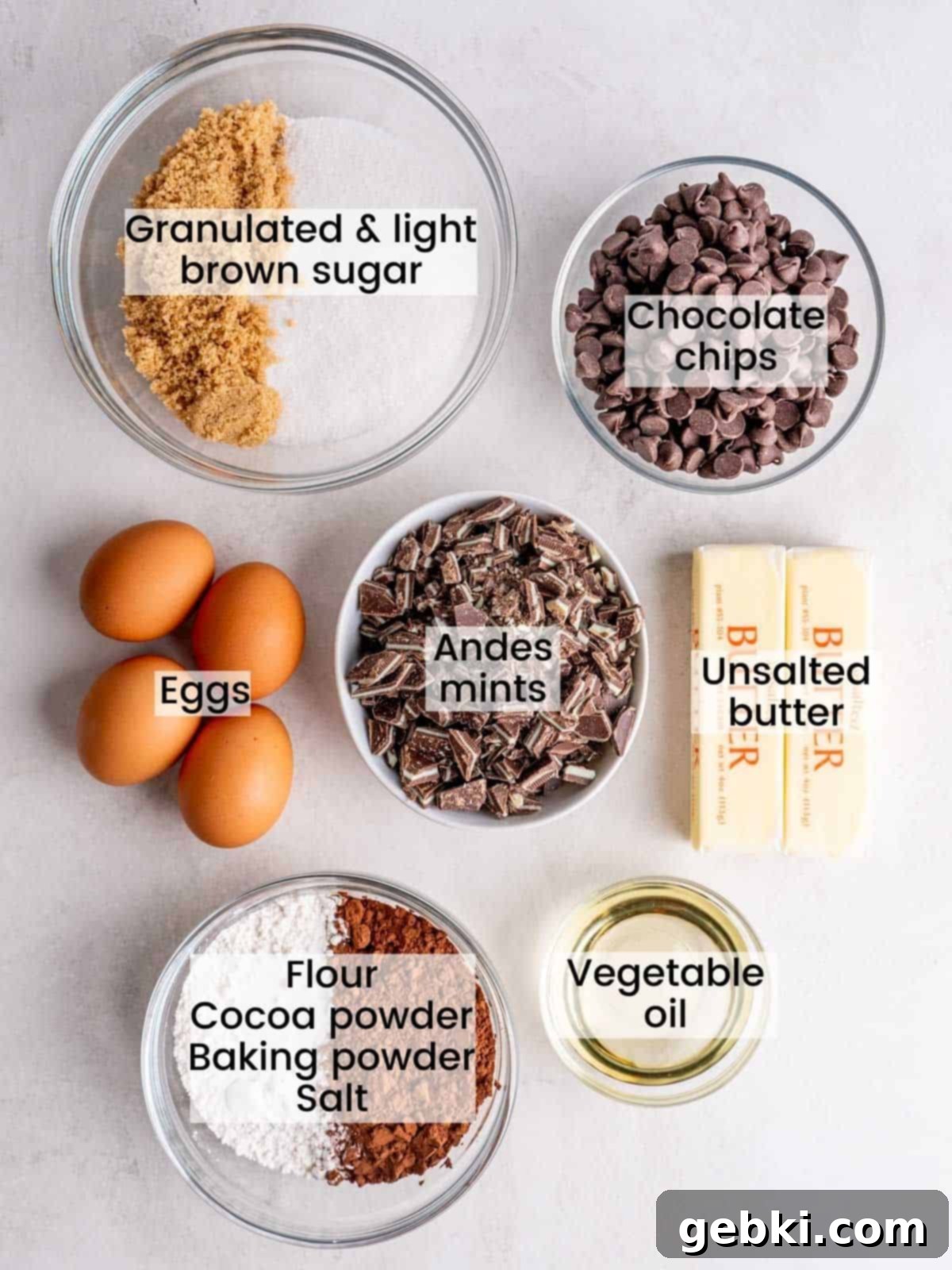 A selection of fresh ingredients laid out, including unsalted butter, semi-sweet chocolate chips, chopped Andes mints, eggs, sugars, cocoa powder, flour, baking powder, and salt, ready for making fudgy mint chocolate brownies.