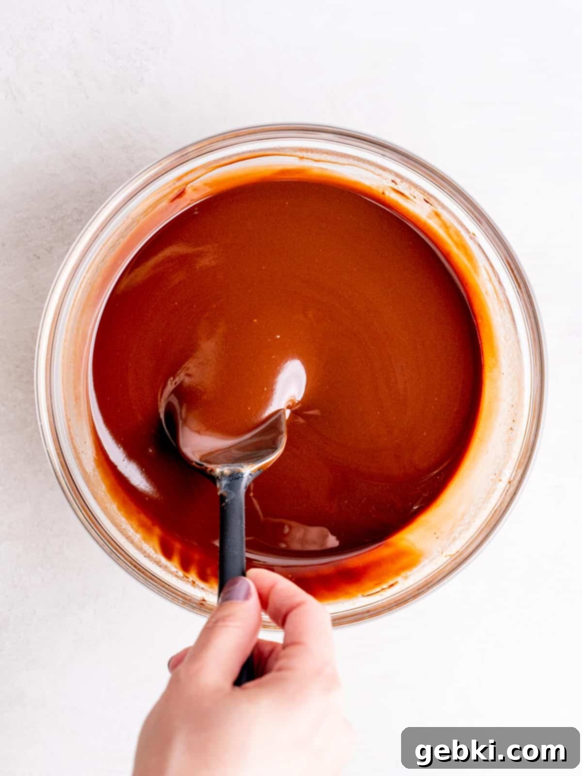 Melted butter, chocolate chips, and Andes mints being stirred in a bowl with a spatula, creating a smooth, glossy chocolate mixture.