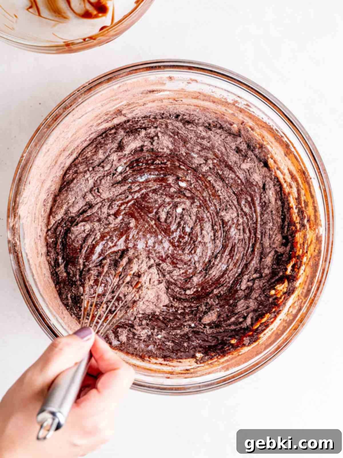 Whisking flour, cocoa powder, baking powder, and salt into a chocolate mixture, ensuring no dry streaks remain.