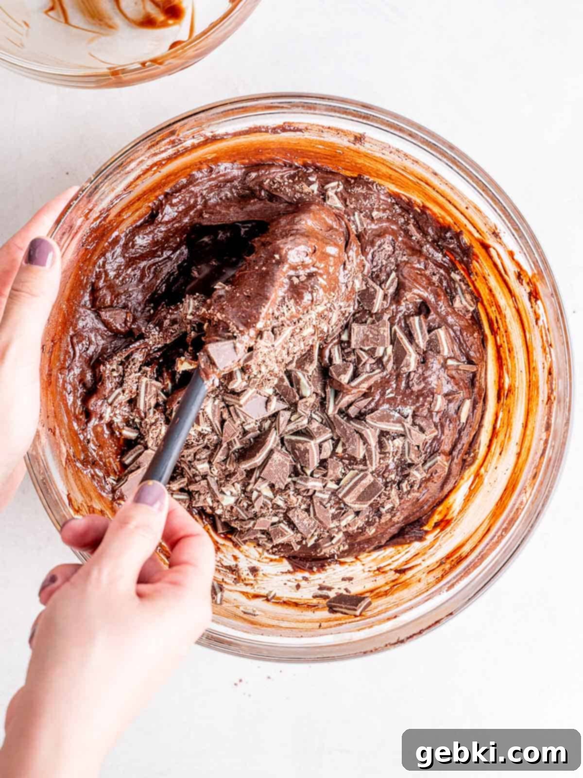 Folding chopped Andes mints into rich brownie batter with a rubber spatula, ensuring even distribution.