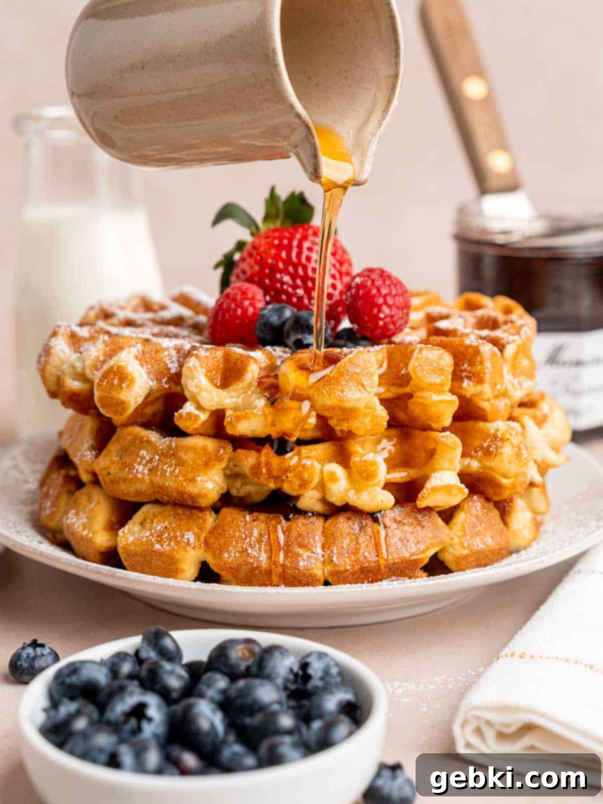 Fluffy Golden Homemade Belgian Waffles 2 Pouring maple syrup on top of a stack of fluffy, golden-brown Belgian waffles, ready for breakfast.