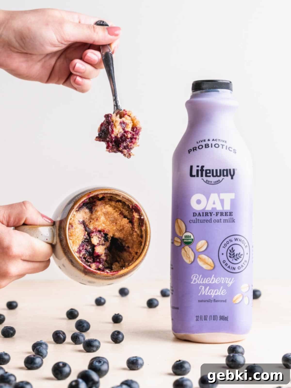 Blueberry Bliss in a Mug 5 A hand holding a blueberry mug muffin next to a bottle of Lifeway Blueberry Maple Oat.