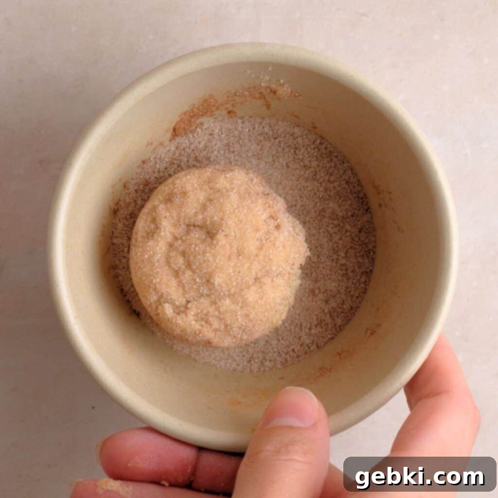 Effortless Sourdough Snickerdoodles 7 Cookie dough balls being coated in cinnamon & sugar mixture, ready for baking.
