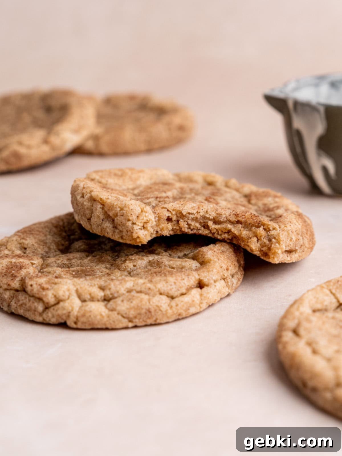 Effortless Sourdough Snickerdoodles 9 Stacked snickerdoodle cookies with a bite taken out of the top cookie, revealing its soft interior.