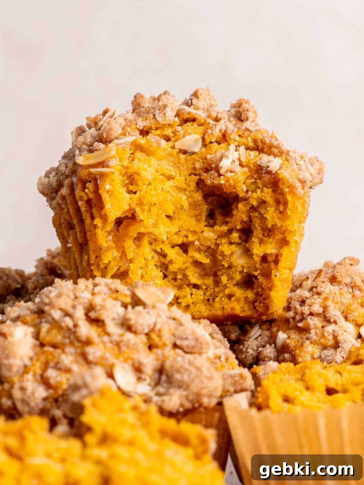 Effortless Pumpkin Oatmeal Muffins with Perfect Crumbly Streusel 2 Freshly baked pumpkin oatmeal muffins with a golden brown cinnamon oat streusel topping, stacked on a plate with one muffin having a bite taken out.