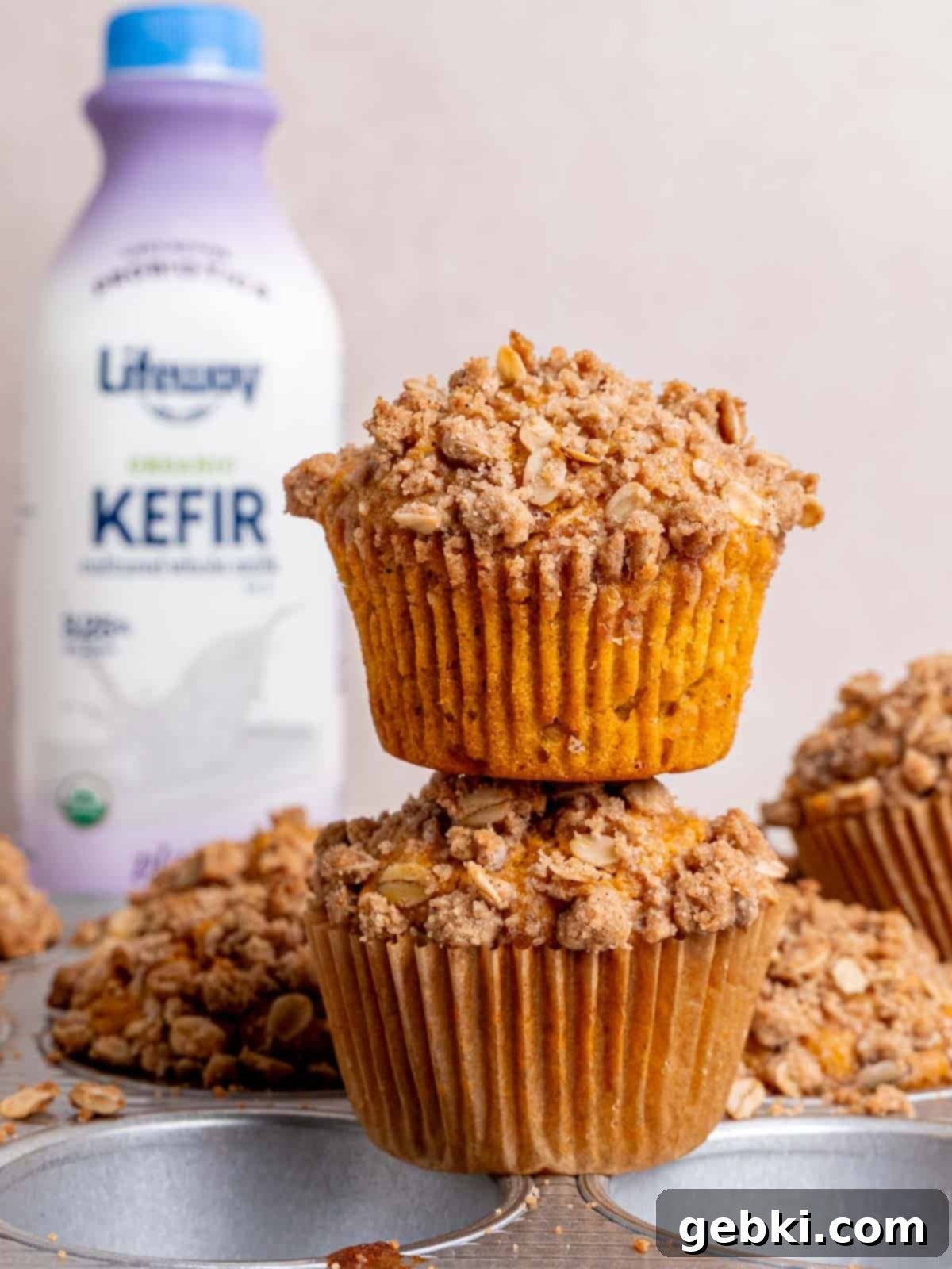 Effortless Pumpkin Oatmeal Muffins with Perfect Crumbly Streusel 12 A close-up of two perfect pumpkin oatmeal muffins with streusel on a plate, with a bottle of Lifeway kefir slightly blurred in the background.