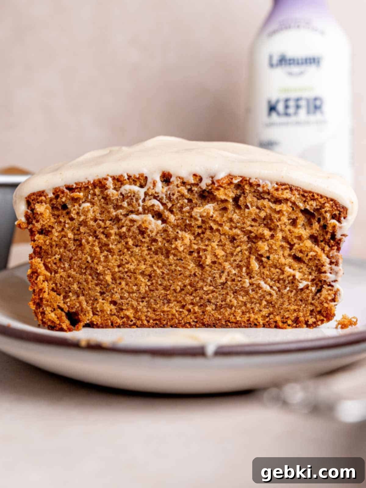Simple Spiced Cake with Decadent Brown Butter Cream Cheese Frosting 11 A loaf of spice cake with cream cheese frosting on top sliced down the middle with a bottle of Lifeway kefir in the background.