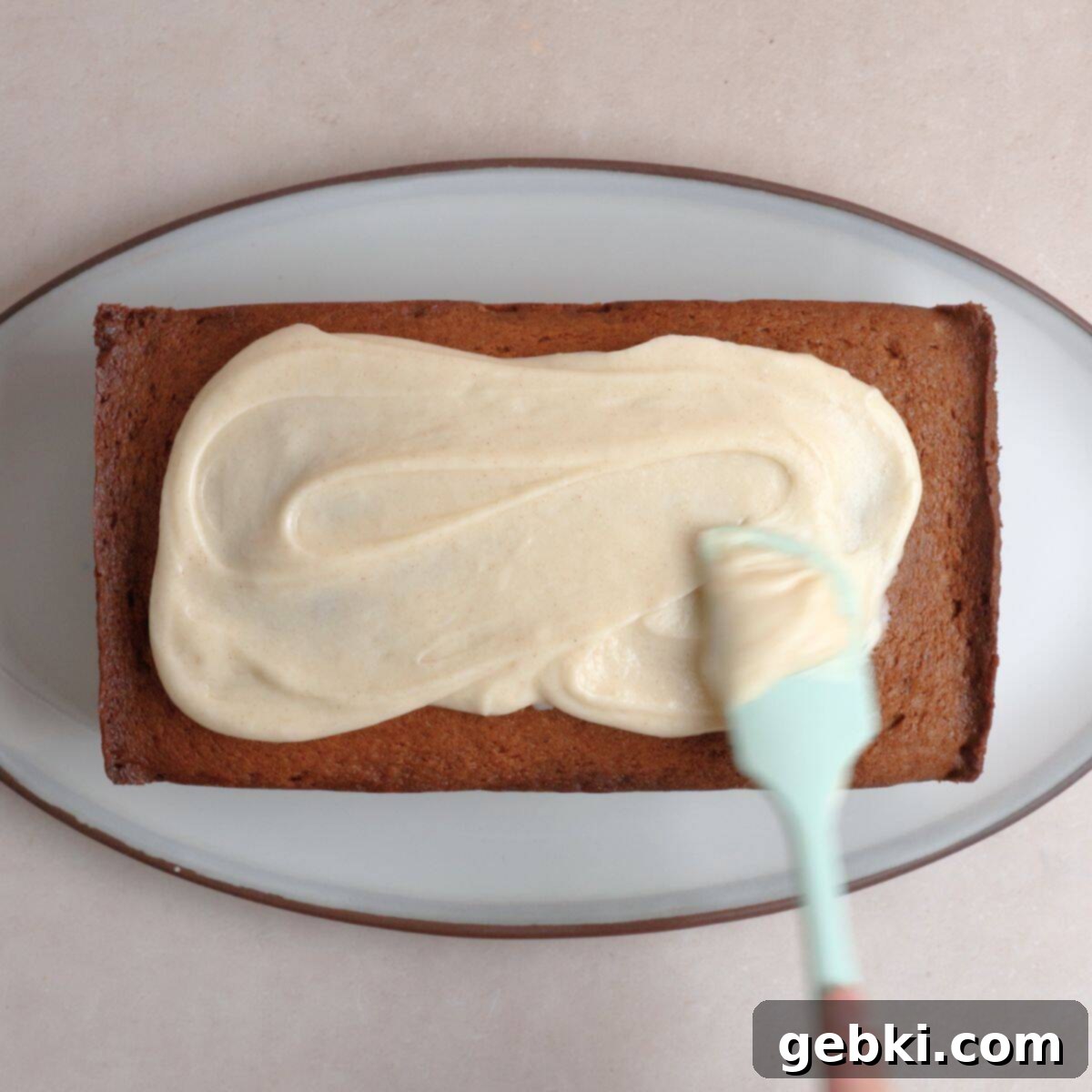 Simple Spiced Cake with Decadent Brown Butter Cream Cheese Frosting 10 Brown butter cream cheese frosting being spread on cooled spice cake using a rubber spatula.