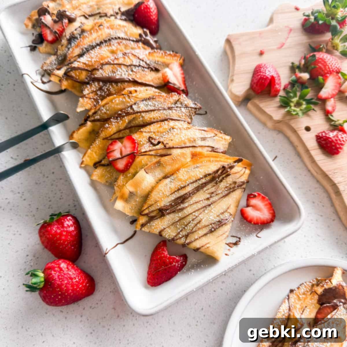 Strawberry Nutella Dream Crepes 2 Strawberry Nutella crepes stacked on a plate, drizzled with chocolate sauce and topped with fresh berries.