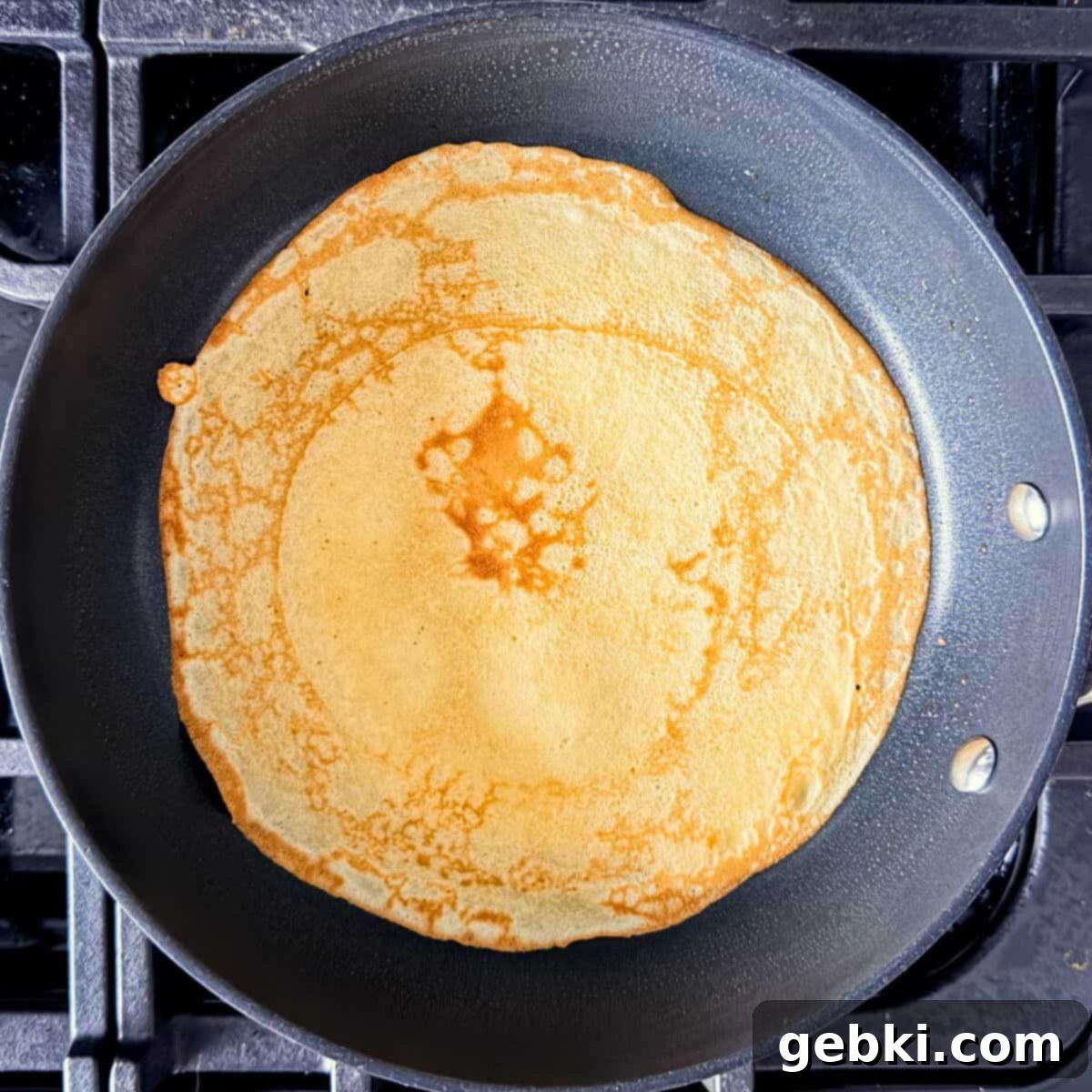 Strawberry Nutella Dream Crepes 7 A golden brown crepe cooking in a pan on the stove.