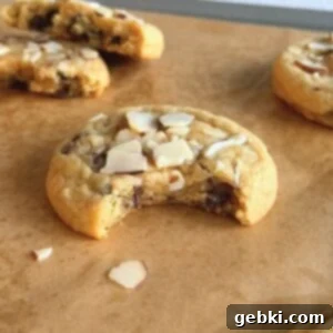 Orange almond chocolate chip cookie on parchment paper with a bite taken out of it.