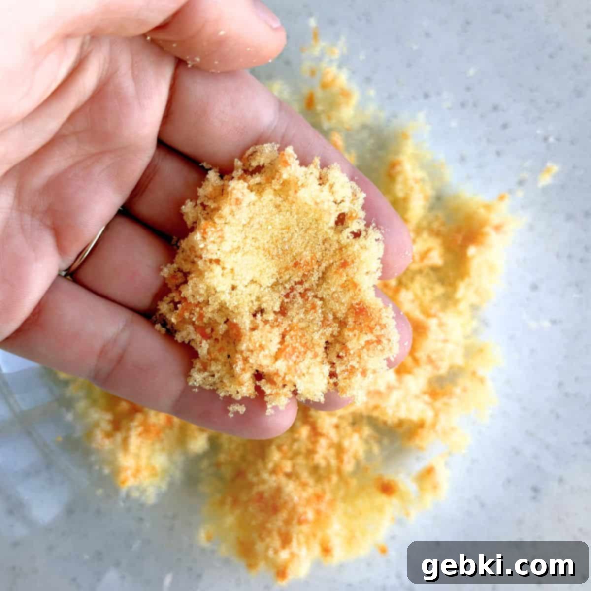 Granulated sugar and orange zest being rubbed together by hand to release the orange oils.